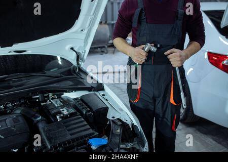 Car service. An auto mechanic is standing near the car with a tool in his hands. Vehicle technical inspection Stock Photo