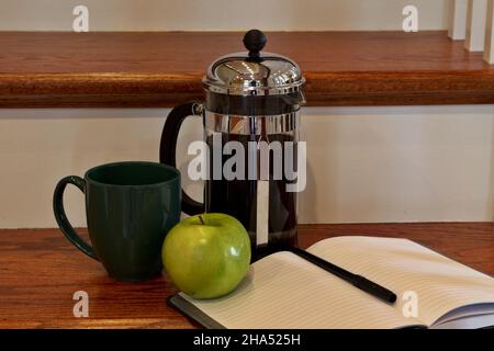 Casual break from writing seen in journal and pen on polished wood step with dark coffee in press, mug, and green apple Stock Photo