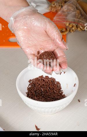 Brigadeiro (brigadier) in a confectioner's hand next to a jar of chocolate sprinkles.g Stock Photo