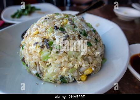 View of a round scoop of vegetable and mushroom fried rice on a small, white plate inside an Asian restaurant Stock Photo