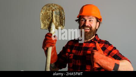 Smiling builder in hardhat with shovel shows thumb up. Workman in work gloves with spade. Copy space Stock Photo