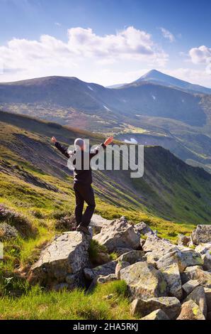 Traveler stands on a rock in the mountains on a sunny day Stock Photo