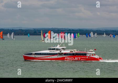isle of wight ferry fast red jet service operated by red funnel ferries passing yachts with colourful sails in the solent during the annual cowes week Stock Photo