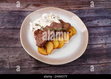 Thick juicy portions of grilled beef fillet with mushroom sauce served with thyme potatoes on an old wooden table Stock Photo