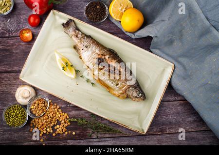 sea bass is served on a plate with lemon, against the background of a wooden table