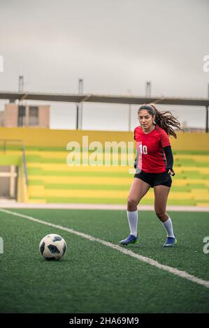 Young female soccer player kicks the ball on the field Stock Photo
