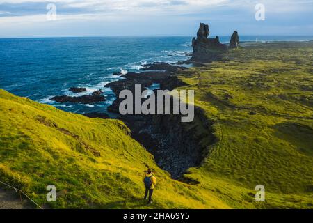 Man hiker in yellow jacket stand on the peak of the rock in outdoor park in Iceland. Londrangar Stock Photo
