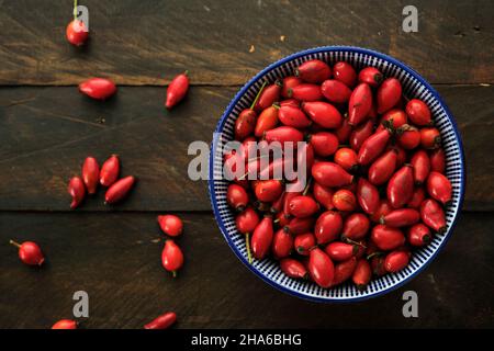 A bowl with dog rose (Rosa Canina) red hips on a rustic wooden table, top view Stock Photo