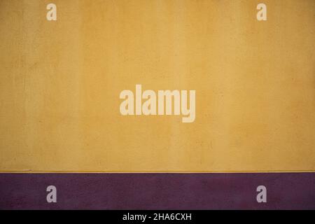 Yellow painted concrete wall with purple colored skirting board Stock Photo