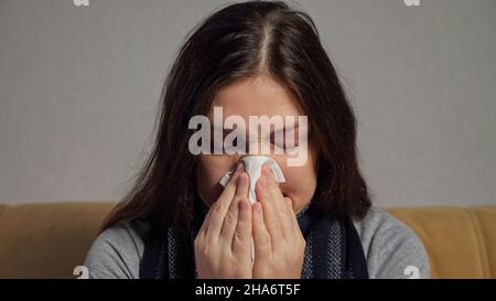Depressed woman with runny nose sits on sofa in living room Stock Photo