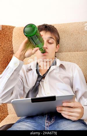 Teenager drinks a Beer with Tablet Computer on the Sofa at the Home Stock Photo