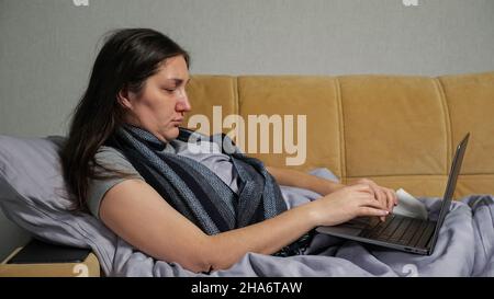 Sick woman with runny nose works distantly using laptop Stock Photo