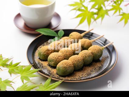 mugwort-flavored rice dumpling covered with soybean flour and green tea served on a black plate set against a white background.  Japanese dumplings. Stock Photo