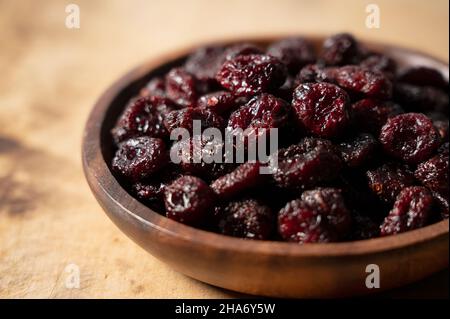Sweet dried cranberries in a wooden bowl against a wooden background. Stock Photo