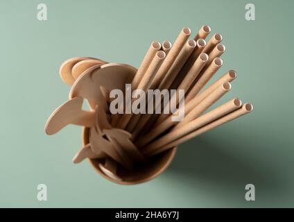 Straws and spoons in disposable paper cups set against a pastel green background. The zero-waste concept. View from above. Stock Photo