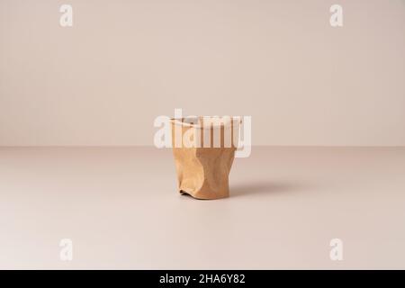 A crushed disposable paper cup on a beige background. Zero-waste concept. Stock Photo