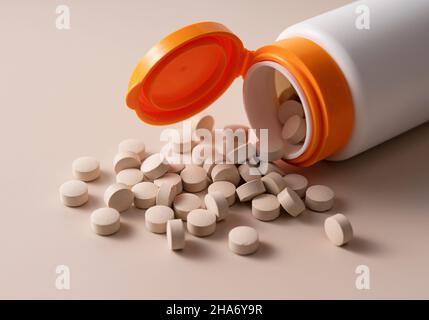 Pills spilling out of bottle on beige background. Concept of pharmaceuticals and supplements. Stock Photo