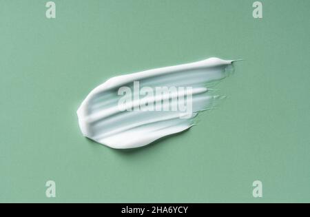 Green White cosmetic cream on green background. Cosmetic BB make up swatch. Drop of liquid foundation strokes. Stock Photo