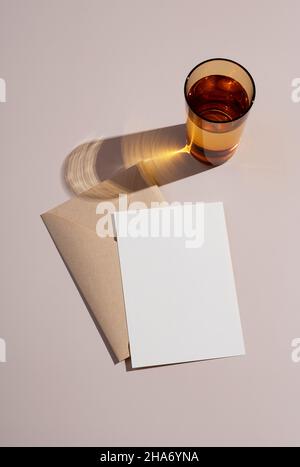 Summer wedding stationery mockup. Beige background with plain greeting cards, invitations and amber glass. Natural light and shadow overlay. Stock Photo