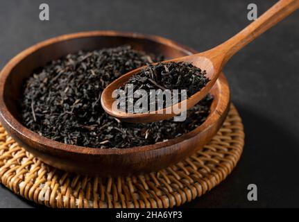 Tea leaves in a wooden plate and spoon on a black background. Scooping tea leaves and holding them up. Stock Photo