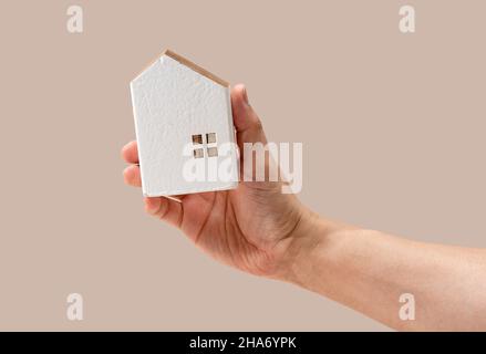 Man's hand holding a model of a house on a beige background. House concept, simple image. Stock Photo