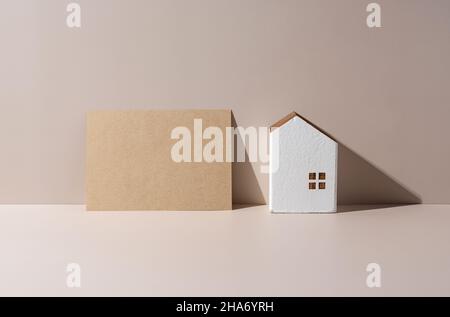 A model of a house on a beige background and a brown card with nothing written on it. Stock Photo