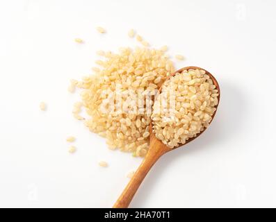 Brown rice in a wooden spoon placed on a white background.  A pile of brown rice. Composition seen from above. Stock Photo