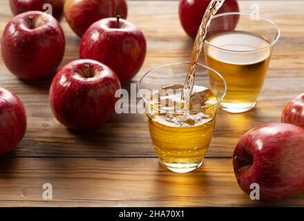 Apple juice in a glass cup against a wooden background. The moment of pouring. Stock Photo
