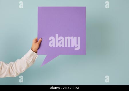 Anonymous man holding square purple mock up speech balloon against blue background Stock Photo