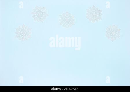 White luminous snowflake decorations on blue. Copy space. Simple winter frame background Stock Photo