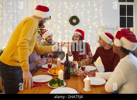 Happy friends sitting at table and eating festive food at Christmas dinner at home Stock Photo