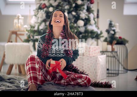 A young girl is excited because of a christmas present while sitting on the floor during christmas holidays at home. Christmas, home, presents Stock Photo