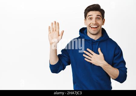 Smiling excited man raising hand up and pointing at himself, introducing, saying hello, standing over white background Stock Photo