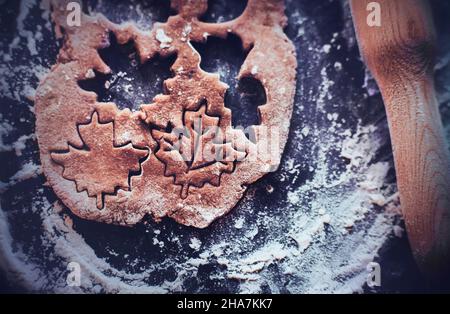 On a baking sheet, sprinkled with flour, there is a wooden rolling pin and dough, from which figures of gingerbread are cut out. Homemade cakes for Ch Stock Photo