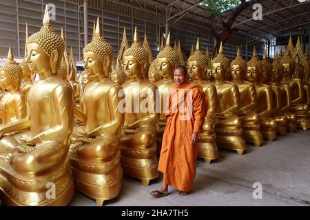 Smiling Buddhist monk passes Buddha statues at a factory for buying  religious objects in Bamrung Muang Road, Bangkok, Thailand,