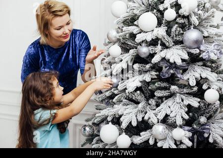 girl and mom decorates Christmas tree with gifts new year lights garland Stock Photo