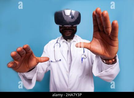 Closeup of moving doctor hands using virtual reality goggles for medical training. Medic in white lab coat with stethoscope using vr headset modern technology for medical investigation. Stock Photo