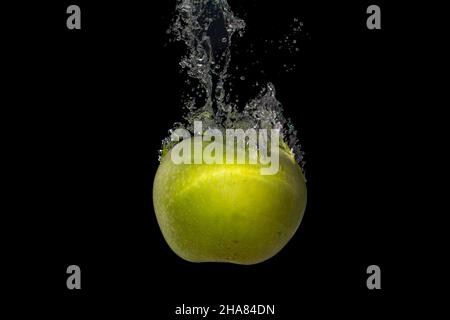 Closeup shot of an apple falls into the water with air bubbles and splashes on s black background Stock Photo