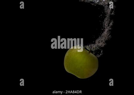 Closeup shot of an apple falls into the water with air bubbles and splashes on s black background Stock Photo
