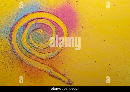 Spiral is drawn on a multicolored, bright powder, on a yellow background. Copy space. Top view.  Stock Photo