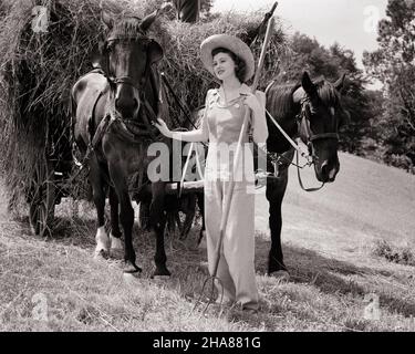 1940s BRUNETTE WOMAN WEARING STRAW HAT AND OVERALLS HOLDING A PITCHFORK AND ONTO THE HARNESS OF HORSE TEAM PULLING A HAY WAGON - h1051 HAR001 HARS STYLE YOUNG ADULT HORSES HAY LIFESTYLE FEMALES JOBS RURAL TRANSPORT COPY SPACE FULL-LENGTH LADIES PERSONS OVERALLS FARMING TEENAGE GIRL WHEELS TRANSPORTATION AGRICULTURE B&W BRUNETTE SKILL OCCUPATION SKILLS MAMMALS PITCHFORK AND FARMERS OCCUPATIONS ONTO HARNESS TEENAGED WAGONS MAMMAL YOUNG ADULT WOMAN BLACK AND WHITE CAUCASIAN ETHNICITY HAR001 OLD FASHIONED Stock Photo