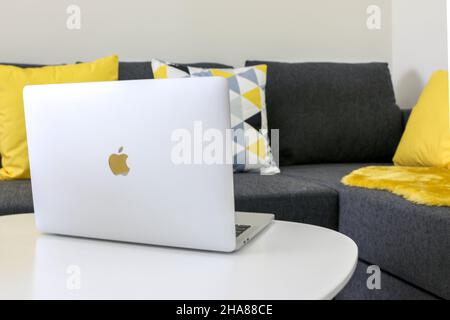 Open Macbook Pro laptop on white wooden table by comfortable grey couch with pillow cushions Stock Photo