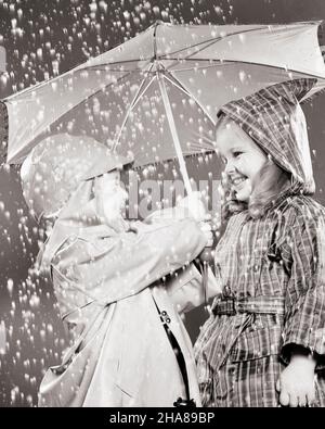 1950s BOY AND GIRL BROTHER AND SISTER SMILING STANDING IN THE RAIN WEARING RAINCOATS AND HOLDING AN UMBRELLA - j5182 HAR001 HARS 1 JUVENILE STYLE WET LAUGH FRIEND PLEASED FAMILIES JOY LIFESTYLE FEMALES BROTHERS STUDIO SHOT HOME LIFE COPY SPACE FRIENDSHIP HALF-LENGTH RAINY PERSONS MALES RAINING SIBLINGS SISTERS B&W RAIL HAPPINESS CHEERFUL AND EXCITEMENT LOW ANGLE SIBLING SMILES CONNECTION MOTION BLUR CONCEPTUAL FRIENDLY JOYFUL STYLISH RAINCOATS BABY BOY GROWTH JUVENILES TOGETHERNESS BLACK AND WHITE CAUCASIAN ETHNICITY HAR001 OLD FASHIONED Stock Photo
