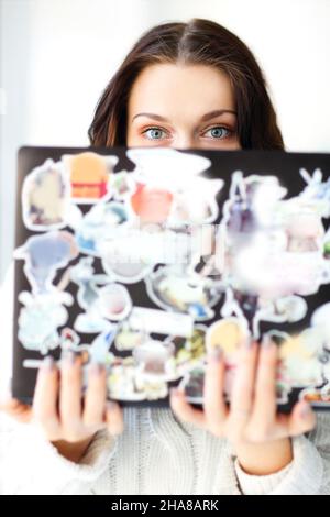 Close up photo of caucasian brunette girl holding open laptop in hands while looking over computer screen into camera with round big shocked blue eyes Stock Photo