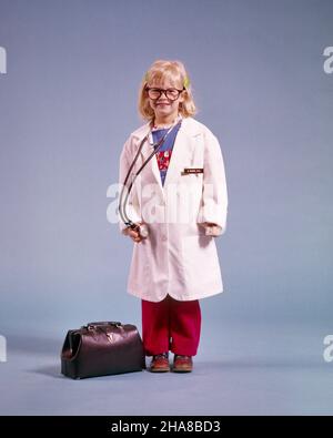 1970s LITTLE BLONDE GIRL DRESSED AS ADULT DOCTOR WEARING EYEGLASSES WHITE LAB COAT STETHOSCOPE BLACK DOCTOR’S BAG AT HER FEET - kj6937 HAR001 HARS COLOR HER SAVING EXPRESSION INJURY OLD TIME FUTURE GRADUATE NOSTALGIA OLD FASHION 1 JUVENILE FACIAL STYLE CAREER BLOND COMPETITION PLEASED JOY LIFESTYLE FEMALES STUDIO SHOT HEALTHINESS ILLNESS COPY SPACE FULL-LENGTH PHYSICAL FITNESS INSPIRATION CARING PROFESSION CONFIDENCE EYEGLASSES STETHOSCOPE EXPRESSIONS EYE CONTACT GOALS HEALTHCARE SUCCESS DREAMS OCCUPATION WELLNESS PREVENTION PROVIDER CHEERFUL DOCTOR'S PROVIDERS HIS PRACTITIONERS STRENGTH Stock Photo