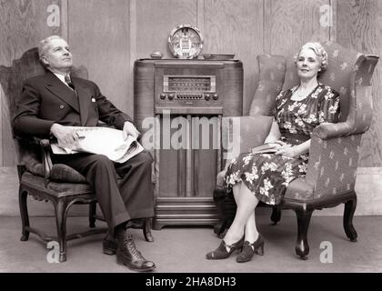 1930s 1940s SENIOR COUPLE SITTING IN CHAIRS LISTENING TO RADIO  - r12954 HAR001 HARS COPY SPACE FRIENDSHIP FULL-LENGTH LADIES PERSONS MALES ENTERTAINMENT SENIOR MAN SENIOR ADULT B&W PARTNER SENIOR WOMAN RADIOS OLD AGE OLDSTERS OLDSTER BROADCASTING LEISURE AUDIO ELDERS CONNECTION STYLISH TOGETHERNESS WIVES BLACK AND WHITE CAUCASIAN ETHNICITY HAR001 OLD FASHIONED Stock Photo