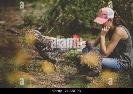 Girl sitting on ground with rooster and hen Stock Photo