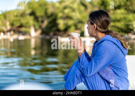 Latin girl with having hot tea by a lake on a summer morning Stock Photo