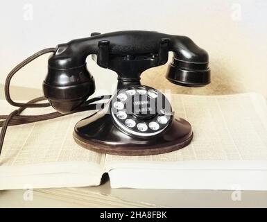1930s OLD BLACK ROTARY DIAL CRADLE TELEPHONE ON OPEN TELEPHONE NUMBER DIRECTORY BOOK - t4320c HAR001 HARS SYNTHETIC Stock Photo
