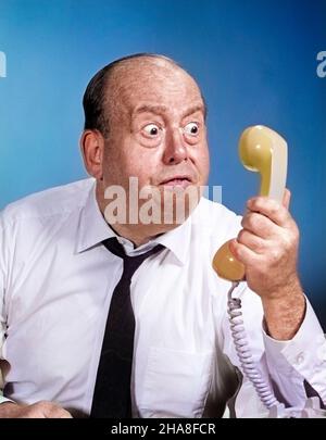 1960s 1970s ANGRY BALDING MAN LOOKING BUG-EYED INTO TELEPHONE RECEIVER - t6073c HAR001 HARS SECRETARY EXECUTIVE EXPRESSION OLD TIME SURPRISE NOSTALGIA OLD FASHION 1 RECEPTIONIST BALD ANGER COMMUNICATION ROUND PANIC ANNOYED PORTRAITS PRESSURE COPY SPACE HALF-LENGTH BLOOD HEAVY SPEAK AMERICANA BUG-EYED DRAMATIC EXCITEMENT BULGING BAD NEWS GRIP CEO FRUSTRATION NECKTIE OCCUPATIONS PHONES BLOOD PRESSURE SNARLING BUSINESS MAN BUSINESS MEN BUSINESS PEOPLE FURY IRRITATION ENRAGED SWEAR TELECOMMUNICATION TELEPHONES BUSINESSPEOPLE BUSINESSPERSON CLOSE-UP FRUSTRATING LONE PANICKY RUMOR MIDDLE AGE FUMING Stock Photo